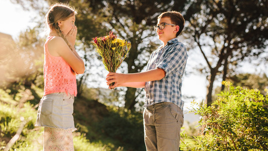 Boy giving a bouquet of flowers to his girlfriend in a park