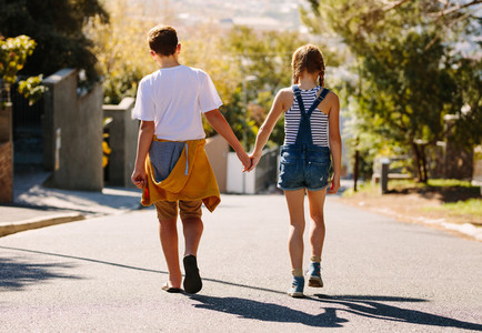 Rear view of kids walking on road holding hands