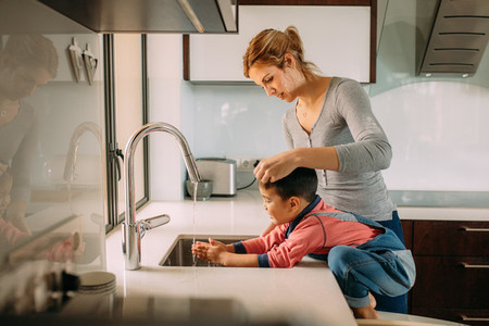 Caring mother and kid wash hands in a sink