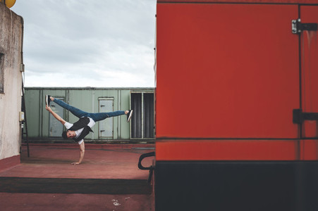 Stylish bboy performing a break dance stance close to red and green machinery in the rooftop of a building