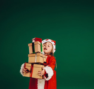 Little girl in santa claus dress carrying gift boxes