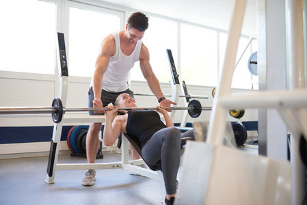 Gym Instructor Supporting Woman in Lifting Barbell