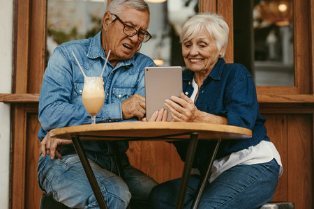Old couple using tablet pc at cafe