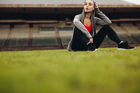 Woman relaxing after workout sitting on grass in stadium