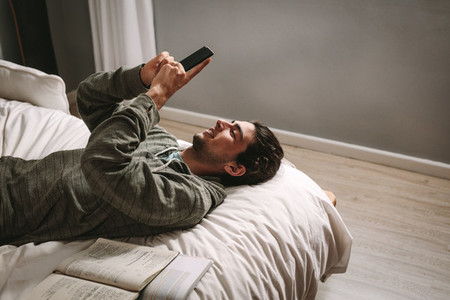 Man looking at mobile phone lying on bed