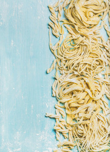 Various homemade uncooked Italian pasta with flour on blue background