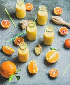 Healthy yellow smoothie with ginger in bottles over grey background