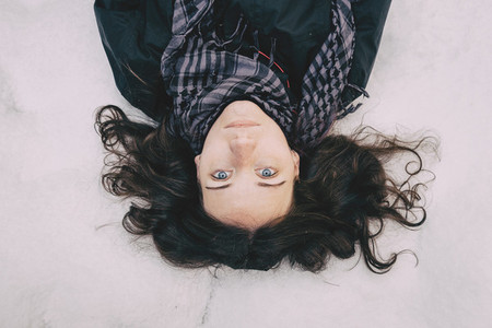 Blue eyed girl lying on top of snow looking at camera