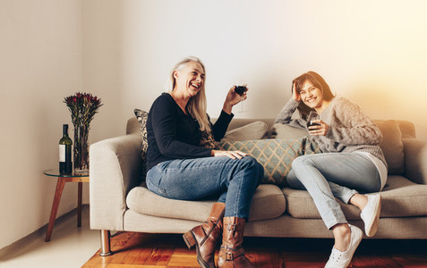 Smiling mother and daughter relaxing on a couch and drinking win