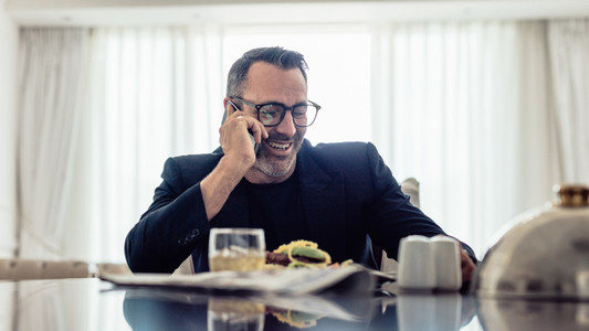 Businessman having lunch and talking on phone in hotel room
