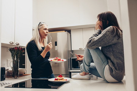 Mother and daughter sitting in kitchen eating cookies