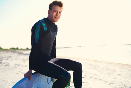 Attractive Surfer Sitting on Edge of his Surfboard