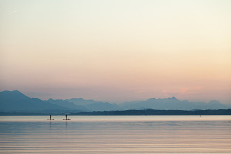A couple practicing paddlesurf at sunset on a lake