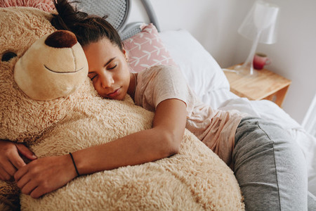 Girl sleeping on bed holding a teddy bear