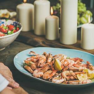 Salad shrimps and candles on wooden table square crop