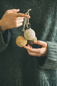 Woman in grey sweater holding decorative golden balls in hands
