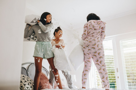 Girls pillow fighting standing on bed