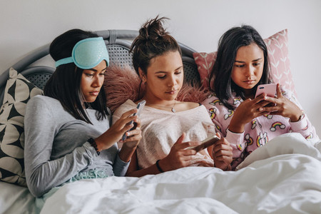 Girls using mobile phone sitting on bed