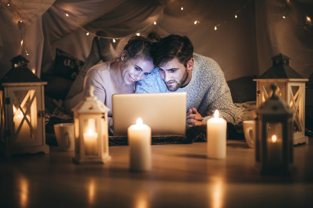 Couple lying on bed looking at a laptop