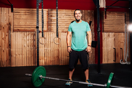 Athletic young smiling man prepares to do some weightlifting exercises with green t shirt