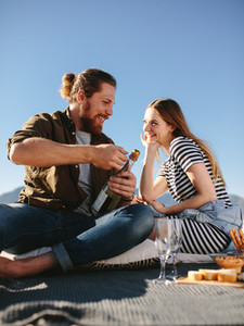 Couple on picnic at the beach opening a champagne bottle