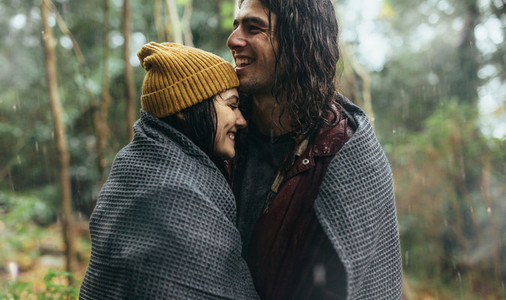 Couple in love standing under the rain wrapped in a blanket