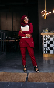 Muslim female standing at coffee shop door with laptop