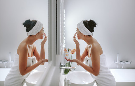 Woman in bathroom applying cosmetic on her face