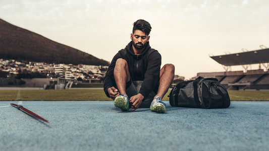 Athlete sitting on running track wearing his shoes