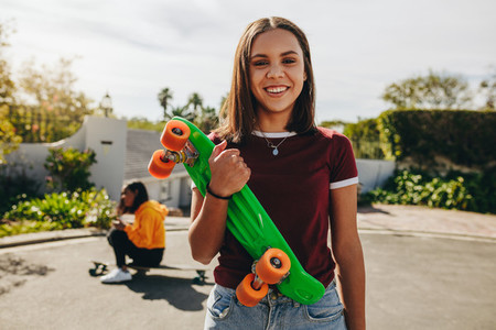 Smiling girl standing on street holding a skateboard