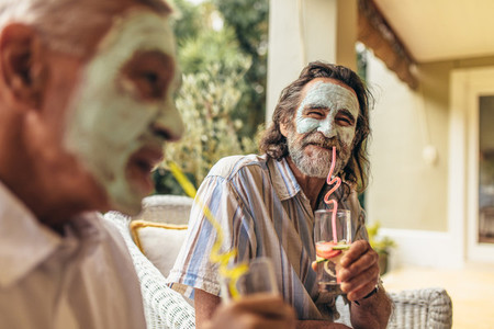 Retired friends with facial clay mask on drinking juice
