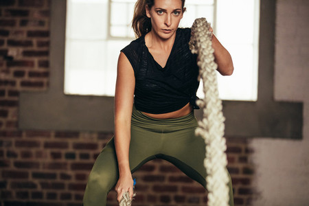 Tough woman working out with battling rope at gym