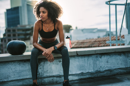 Female athlete relaxing on rooftop fence during workout