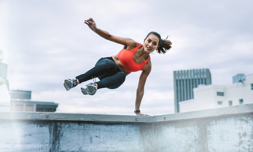 Woman athlete jumping onto the rooftop from the fence