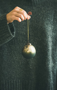 Woman in grey sweater holding decorative golden ball in hand