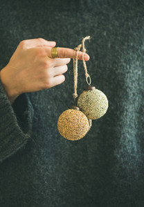 Woman in grey sweater holding decorative golden balls on finger