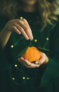 Fresh tangerine fruit in hands of girl wearing green dress