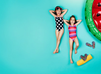Small girls in swimwear relaxing on blue background