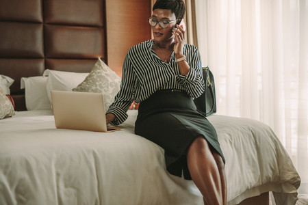 Business woman in hotel room using laptop and smartphone