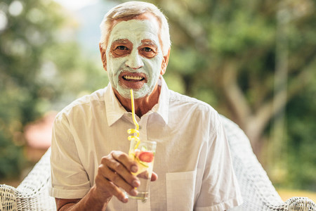 Fully elderly man with clay mask on face having juice