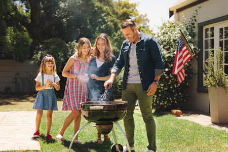 Couple standing with their kids in their backyard making barbequ