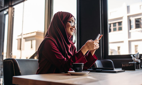Woman in hijab sitting at cafe using mobile phone