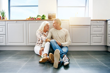Affectionate senior couple sitting together on their kitchen floor