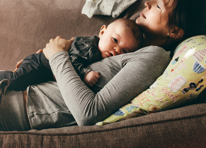 Woman lying on couch with eyes closed holding her baby