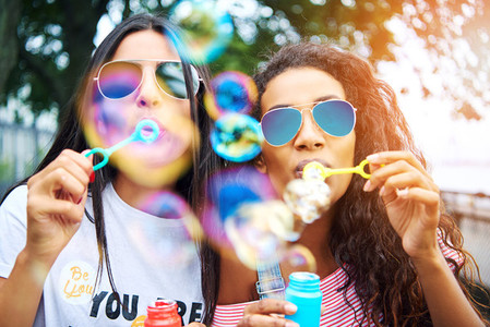 Carefree girlfriends playing with bubble wands outside in summer