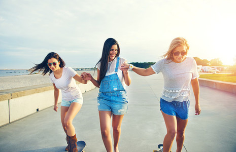 Three young cheerful girls skateboarding in sunlight