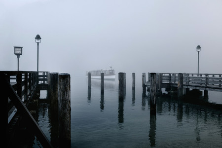 Views of the wooden pier in the mist and a lone boat on the Konigsee lake of Germany