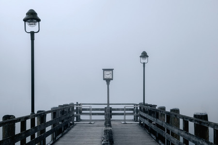 Views of the lonely wooden pier in the fog with two streetlights and ancient clock