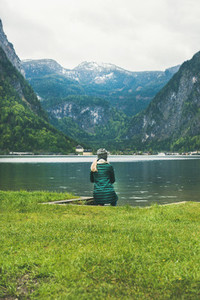 Female traveller sitting at mountain lake coast in the Alps