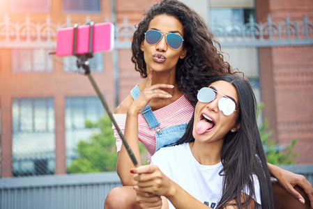 Carefree girlfriends making faces and taking selfies outside